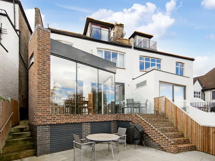 Connaught rear extension on a sloping site, with frameless glazed corner above a brick plinth