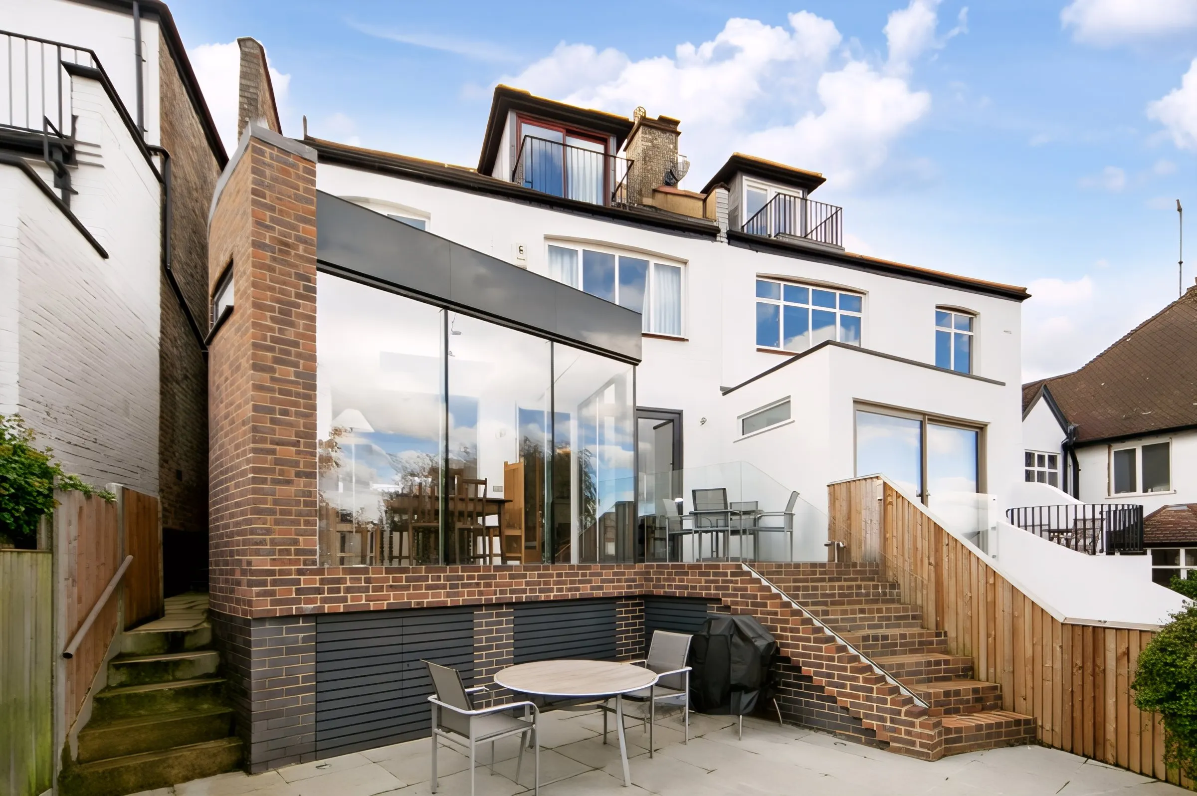 Connaught rear extension on a sloping site, with frameless glazed corner above a brick plinth