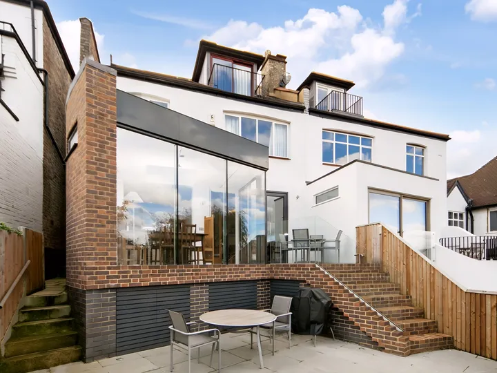 Connaught rear extension on a sloping site, with frameless glazed corner above a brick plinth