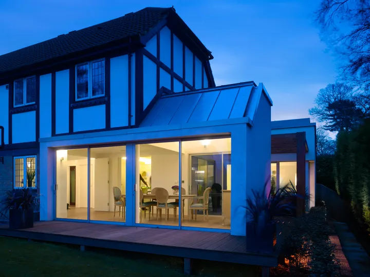Rear extension of the 1990s house at dusk, lit from inside