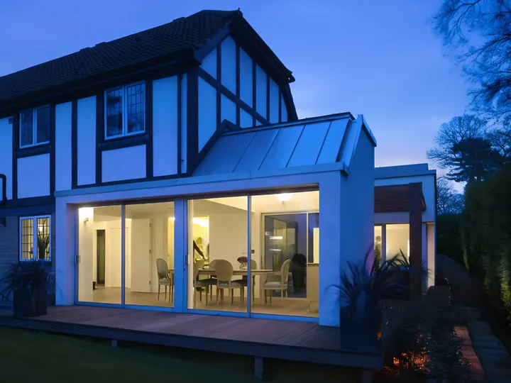 Rear extension of the 1990s house at dusk, lit from inside